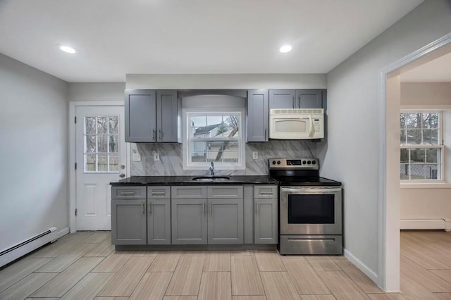 kitchen with electric stove, decorative backsplash, baseboard heating, dark stone countertops, and sink