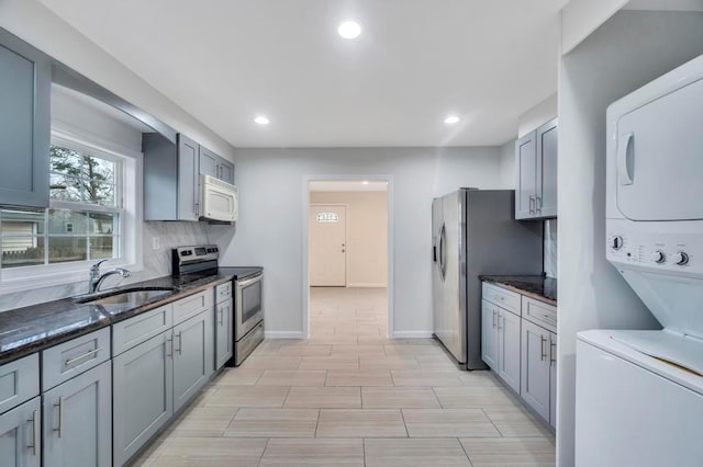 kitchen featuring dark stone countertops, stainless steel appliances, stacked washer and clothes dryer, sink, and tasteful backsplash