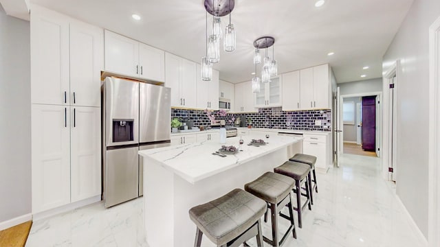 kitchen featuring light stone countertops, appliances with stainless steel finishes, decorative light fixtures, white cabinets, and a center island