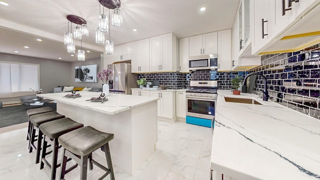 kitchen with hanging light fixtures, sink, appliances with stainless steel finishes, a kitchen island, and white cabinetry