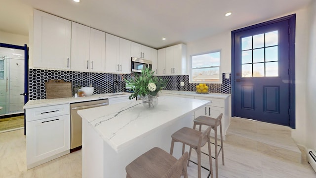 kitchen with white cabinetry, a baseboard radiator, light stone counters, a kitchen island, and appliances with stainless steel finishes