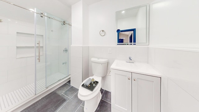 bathroom with vanity, a shower with door, toilet, and tile walls