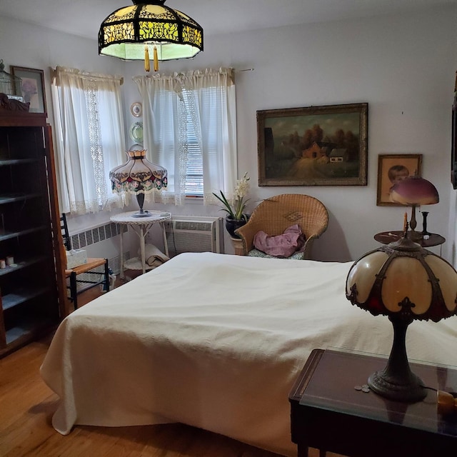 bedroom with radiator, a wall mounted AC, multiple windows, and wood-type flooring