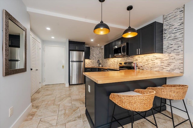 kitchen featuring stainless steel appliances, wood counters, backsplash, kitchen peninsula, and a breakfast bar area