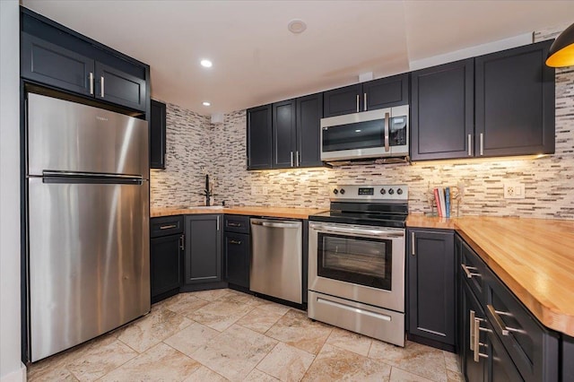 kitchen with butcher block countertops, decorative backsplash, sink, and appliances with stainless steel finishes