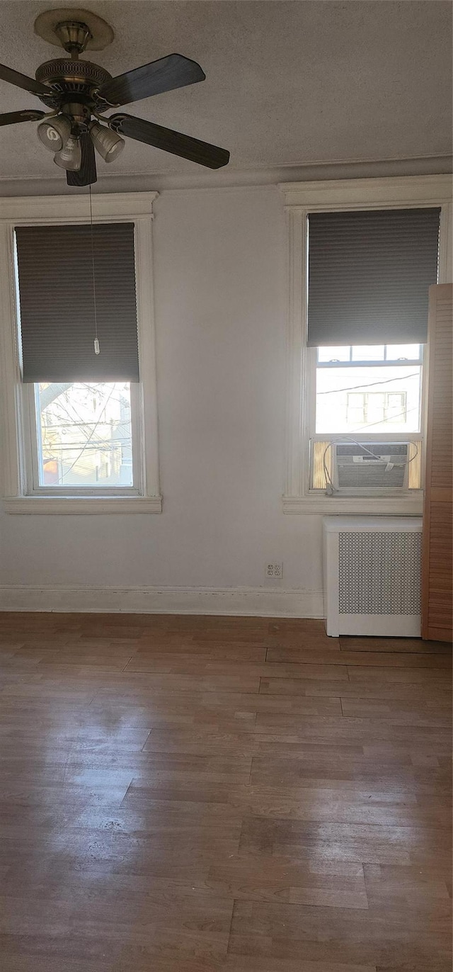 unfurnished room featuring light hardwood / wood-style floors, ceiling fan, cooling unit, and radiator