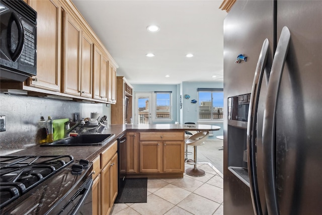 kitchen featuring black appliances, kitchen peninsula, sink, a kitchen breakfast bar, and light tile patterned floors