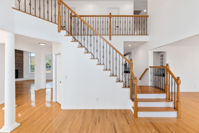 stairway with hardwood / wood-style flooring, ornate columns, a high ceiling, and a stone fireplace