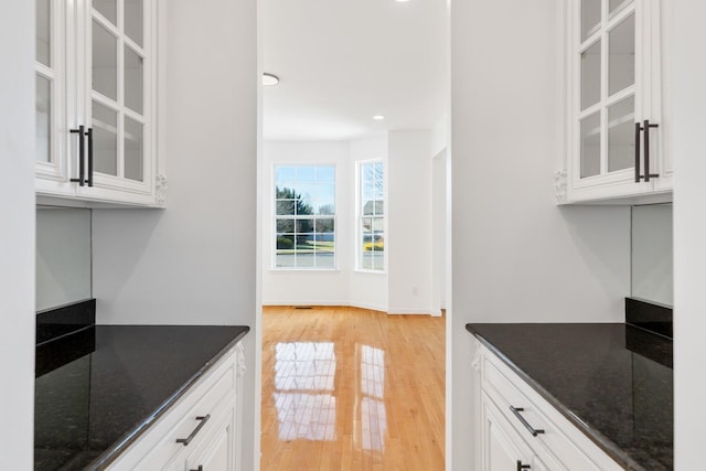 kitchen with light wood-type flooring, dark stone countertops, and white cabinetry