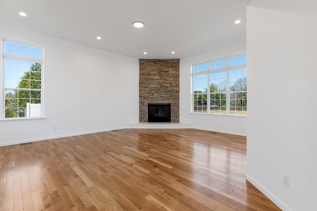 unfurnished living room featuring a healthy amount of sunlight, light wood-type flooring, and a stone fireplace