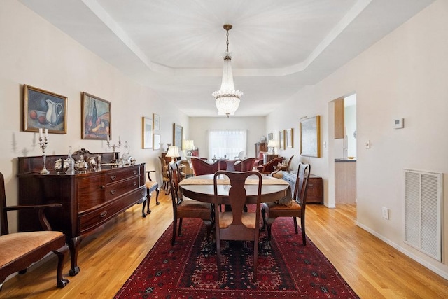 dining space featuring light wood-type flooring, a chandelier, and a raised ceiling