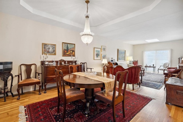 dining space with a chandelier, light hardwood / wood-style floors, and a raised ceiling