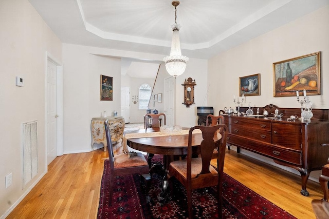 dining area with a tray ceiling, light hardwood / wood-style flooring, and a chandelier