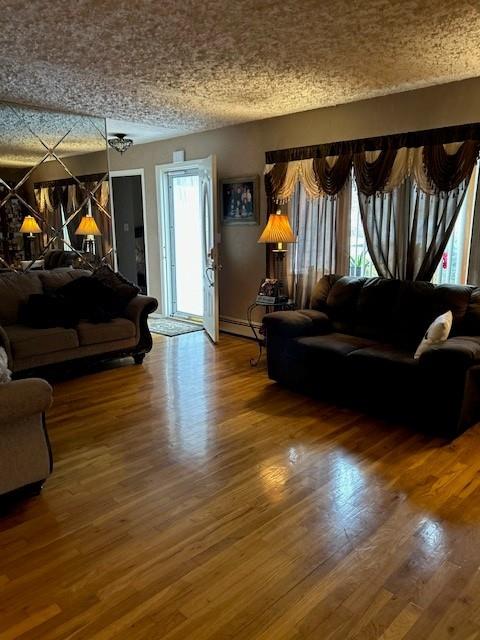 living room with a baseboard heating unit, a textured ceiling, and wood-type flooring