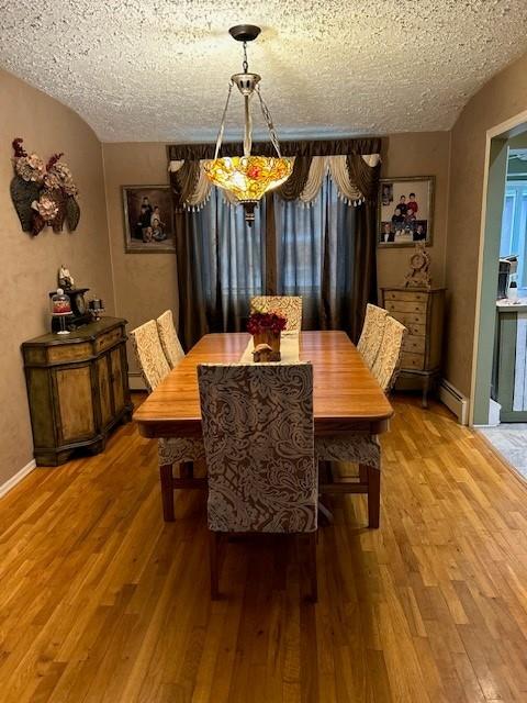 dining space featuring a baseboard radiator, a textured ceiling, and hardwood / wood-style flooring