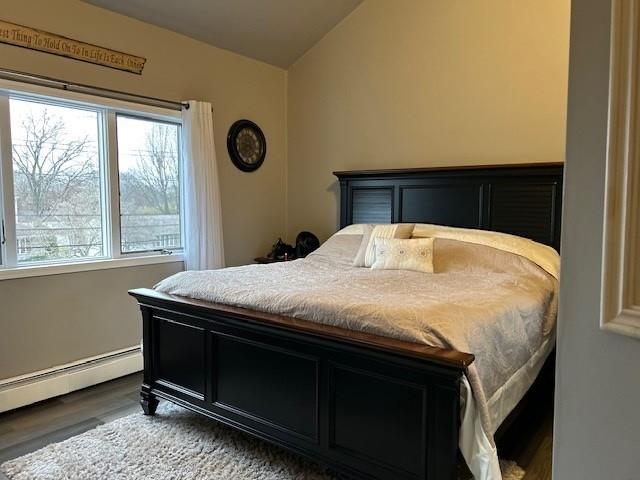 bedroom featuring wood-type flooring, vaulted ceiling, multiple windows, and a baseboard heating unit