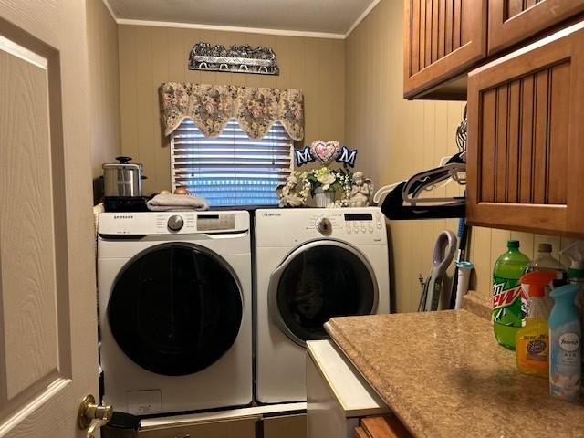 laundry area featuring wood walls, cabinets, ornamental molding, and washer and clothes dryer