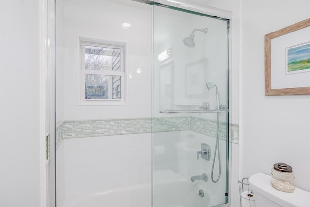 bathroom featuring toilet and bath / shower combo with glass door