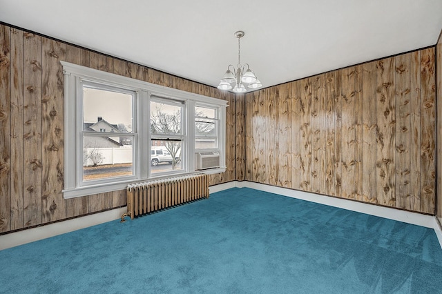 carpeted empty room with radiator, a notable chandelier, a healthy amount of sunlight, and wood walls