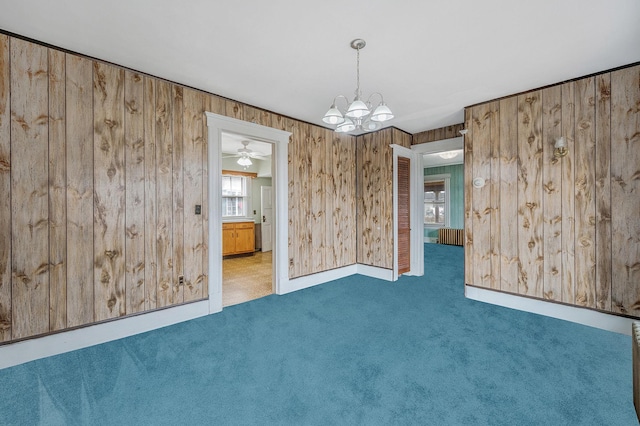 carpeted empty room featuring radiator, a chandelier, and wood walls