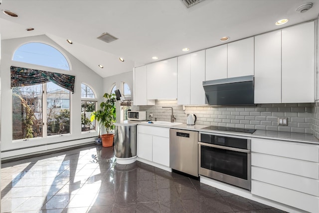 kitchen featuring vaulted ceiling, baseboard heating, white cabinets, appliances with stainless steel finishes, and sink