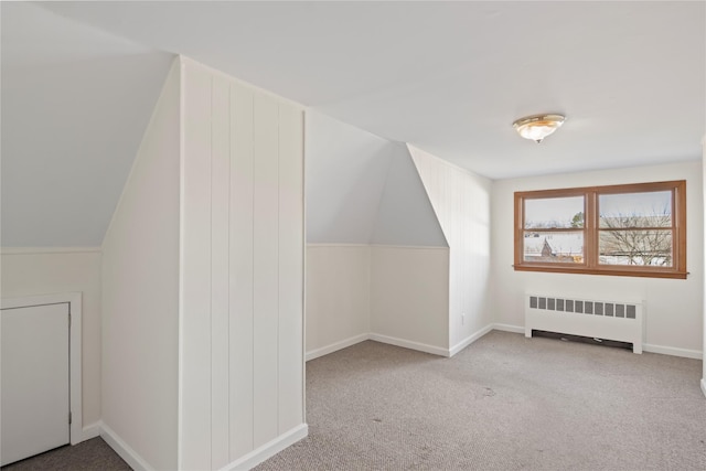 additional living space featuring radiator heating unit, light colored carpet, and vaulted ceiling