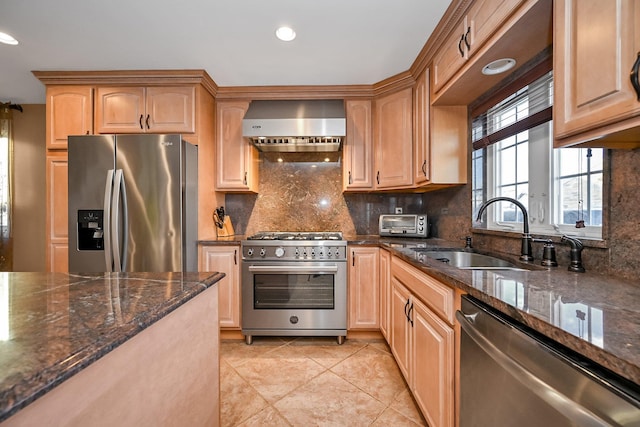 kitchen featuring sink, dark stone counters, wall chimney range hood, and stainless steel appliances