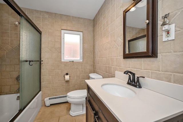 full bathroom with tile walls, baseboard heating, shower / bath combination with glass door, tile patterned floors, and vanity