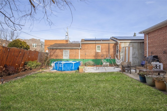 back of house with a covered pool, a lawn, solar panels, and a patio