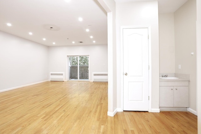 unfurnished living room featuring sink, radiator heating unit, and light wood-type flooring