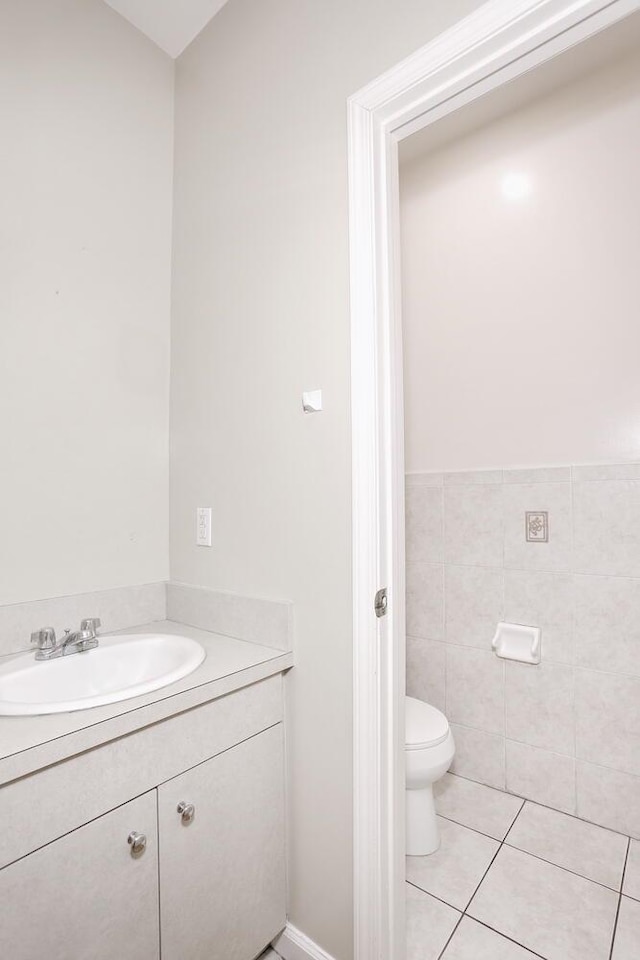 bathroom with toilet, tile patterned flooring, tile walls, and vanity