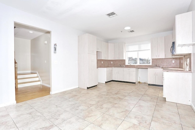 kitchen with sink, light tile patterned flooring, white cabinetry, and backsplash