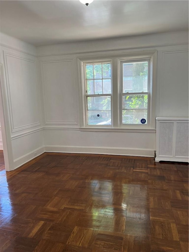 empty room with dark parquet flooring and radiator