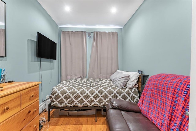 bedroom with a baseboard heating unit and wood-type flooring