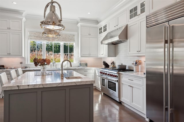 kitchen featuring high quality appliances, light stone countertops, a kitchen island with sink, and hanging light fixtures