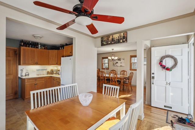 dining area with crown molding, ceiling fan with notable chandelier, and light wood-type flooring