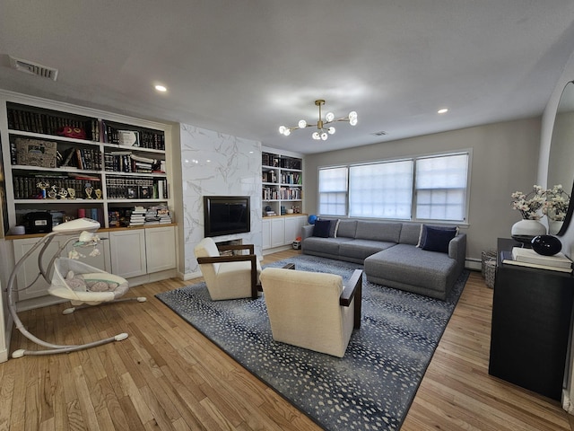 living room featuring a baseboard radiator, a notable chandelier, a high end fireplace, light wood-type flooring, and built in shelves