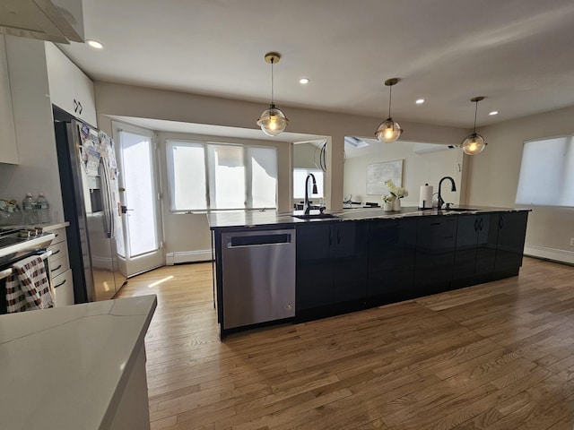 kitchen with white cabinetry, an island with sink, hanging light fixtures, baseboard heating, and stainless steel appliances