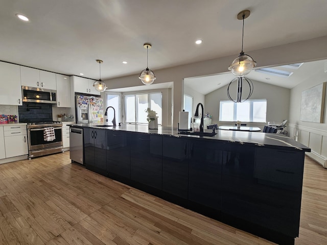 kitchen with pendant lighting, sink, white cabinetry, stainless steel appliances, and a large island with sink