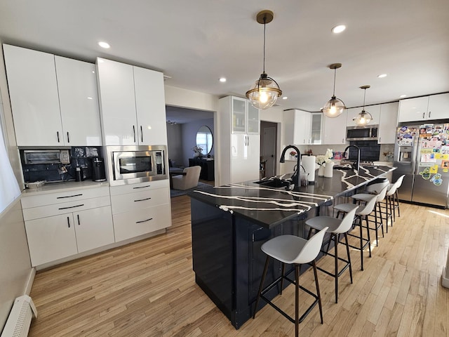 kitchen featuring sink, white cabinetry, decorative light fixtures, baseboard heating, and stainless steel appliances