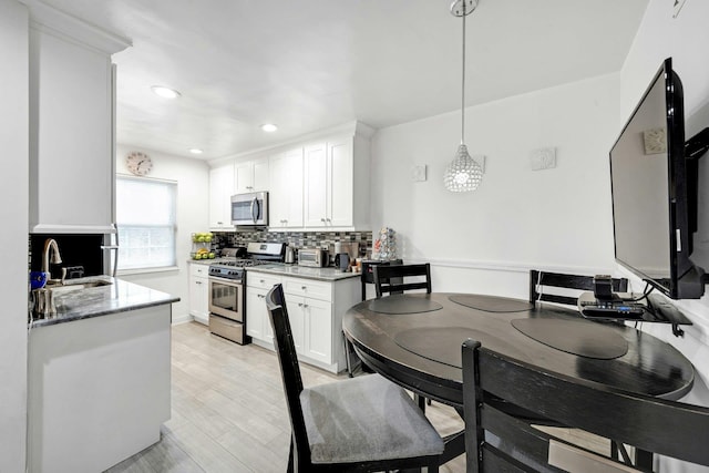 kitchen with stainless steel appliances, stone counters, sink, white cabinetry, and decorative light fixtures