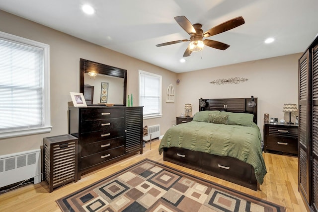 bedroom with ceiling fan, light hardwood / wood-style floors, multiple windows, and radiator