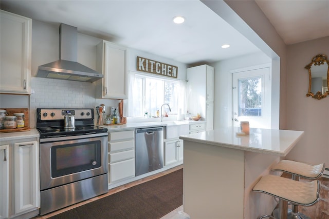 kitchen with white cabinets, wall chimney range hood, stainless steel appliances, and a kitchen island