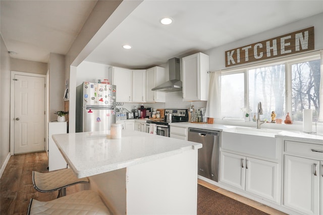 kitchen featuring a kitchen island, white cabinetry, appliances with stainless steel finishes, wall chimney exhaust hood, and light stone counters