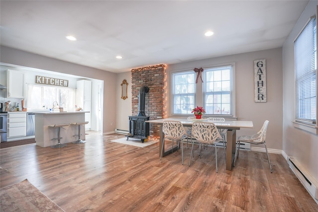 dining space with light hardwood / wood-style floors, a wood stove, and a baseboard radiator