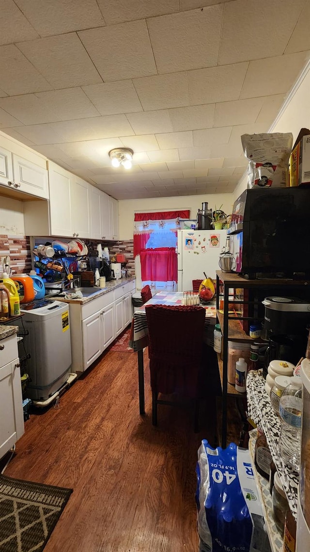 kitchen with washer / dryer, freestanding refrigerator, dark wood-style flooring, and white cabinetry