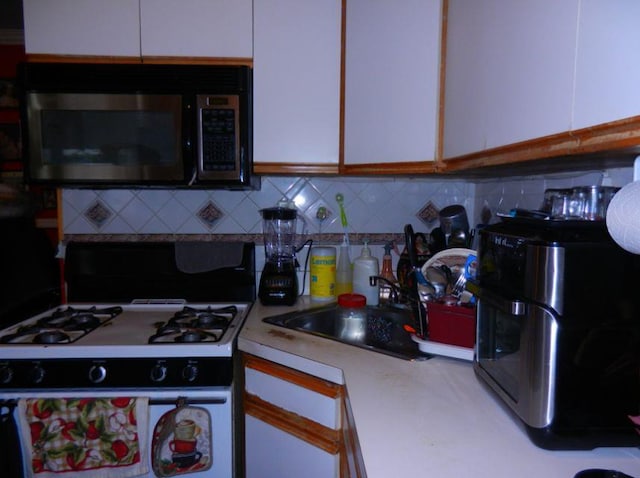 kitchen with white cabinets, backsplash, white gas range, and sink