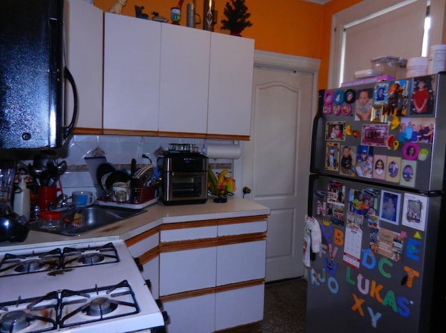 kitchen featuring backsplash, white range with gas cooktop, white cabinets, and fridge