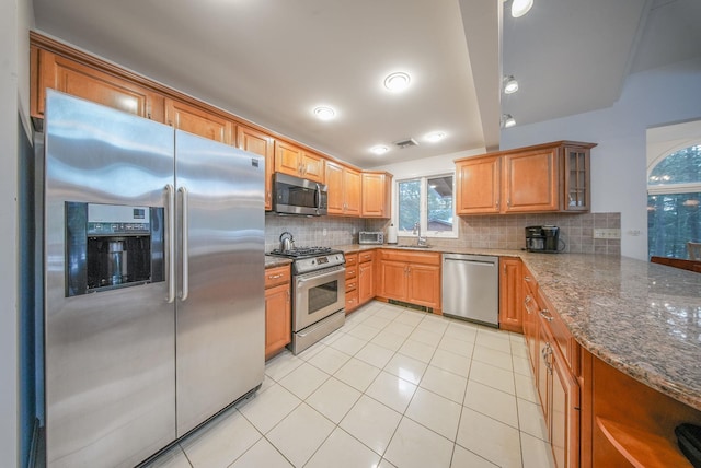 kitchen featuring dark stone countertops, stainless steel appliances, decorative backsplash, sink, and light tile patterned flooring