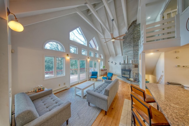 living room with baseboard heating, a stone fireplace, light hardwood / wood-style floors, beamed ceiling, and high vaulted ceiling